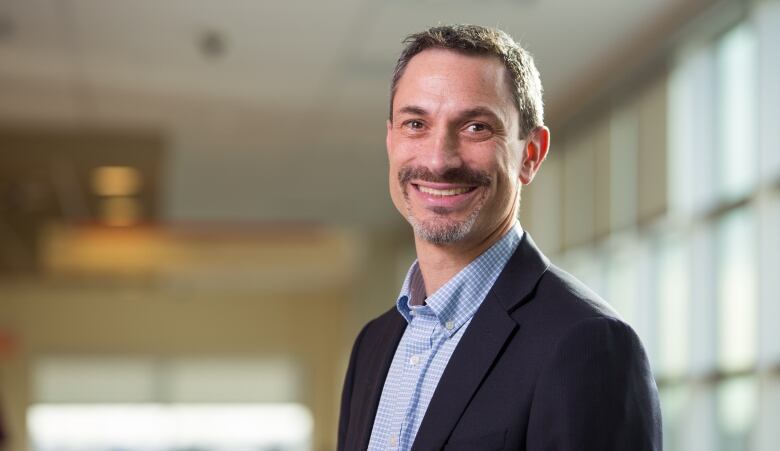 A headshot of a professor and doctor in what looks like a hospital or university hallway.