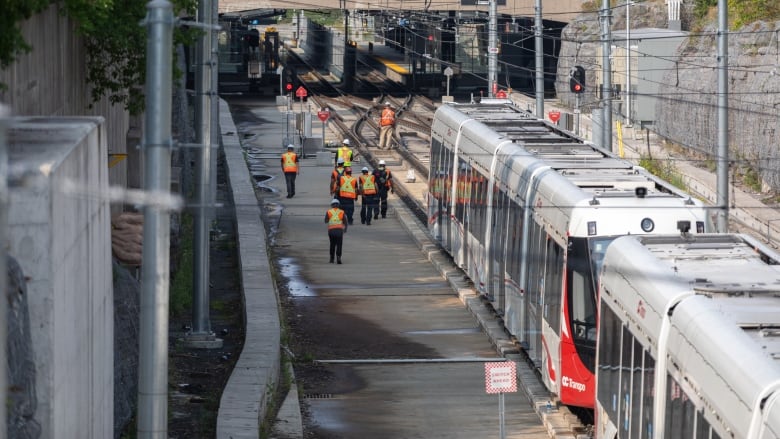 A photo of crews walking along the LRT on Aug. 9, 2021. It shows an out-of-service LRT train that derailed after an axle broke. 