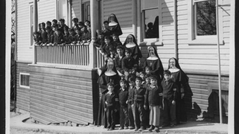 A black-and-white picture of a group of nuns, lined up along with dozens of Indigenous kids.