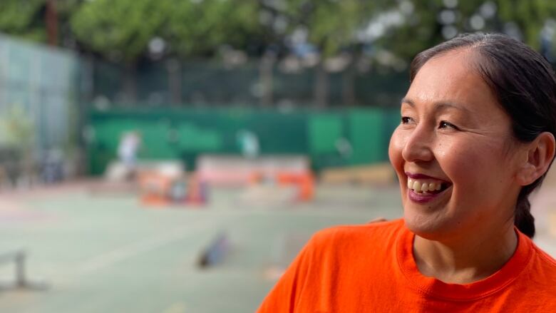 A woman in an orange shirt smiles at a skate park.