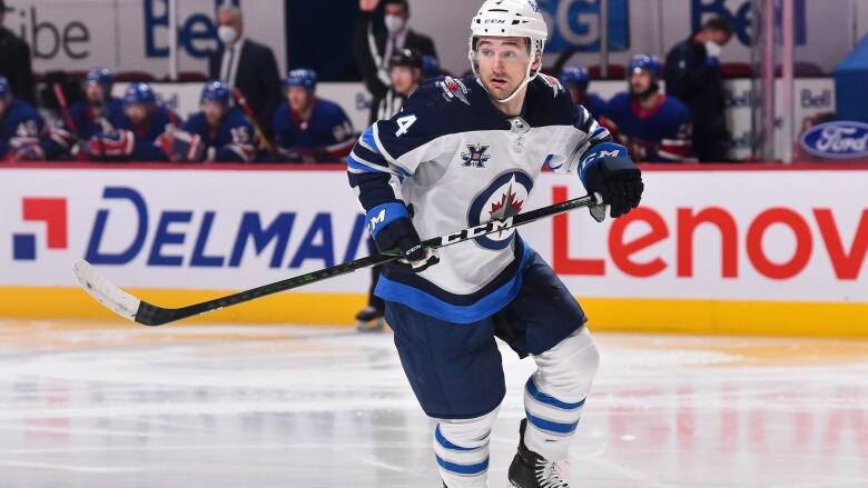 Man in blue and white hockey uniform skates on ice, he is holfing a hockey stick. 