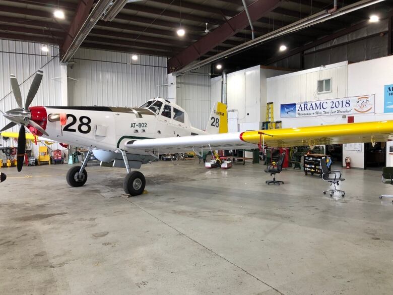 Asmall white plane with yellow wings and a nose prop sits in a hangar.