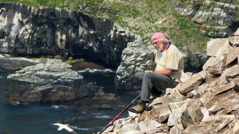 A man sitting on a rocky cliffside near an ocean. 