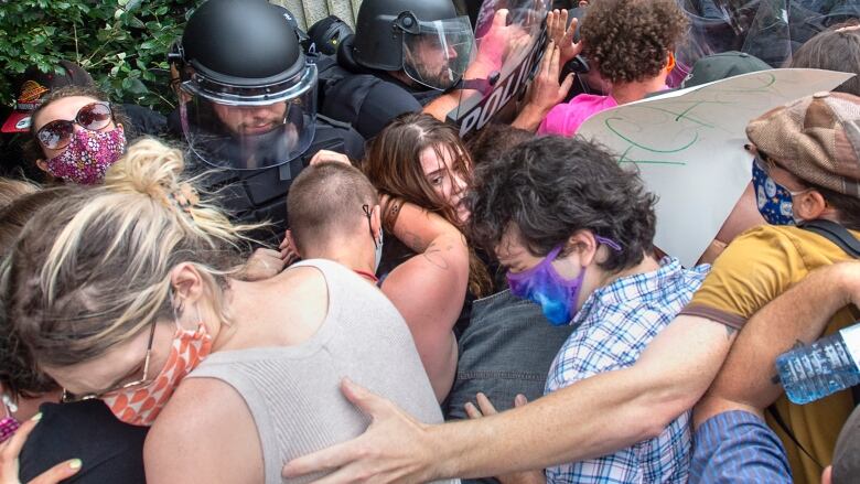 People wearing masks push against a line of police officers in riot gear.