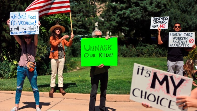 People at a protest hold signs with anti-vaccine-mandate messages such as 'We don't need no vaccinations' and 'Unmask our kids.'