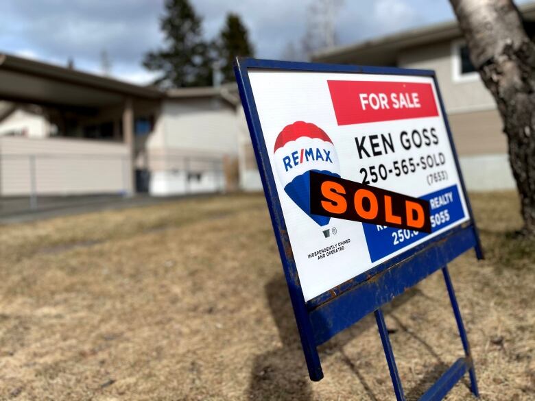 A 'For Sale' sign outside a single-family home.