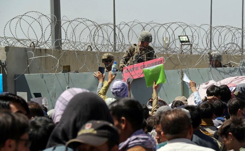 A U.S. soldier holds a sign indicating a gate is closed as hundreds of people gather some holding documents, near an evacuation control checkpoint on the perimeter of the Hamid Karzai International Airport, in Kabul, Afghanistan, Thursday, Aug. 26, 2021. Western nations warned Thursday of a possible attack on Kabuls airport, where thousands have flocked as they try to flee Taliban-controlled Afghanistan in the waning days of a massive airlift. Britain said an attack could come within hours. 