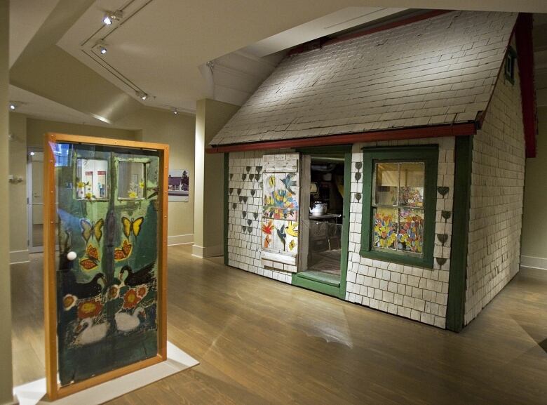 A tiny house with white shingles and green trim inside a gallery building.