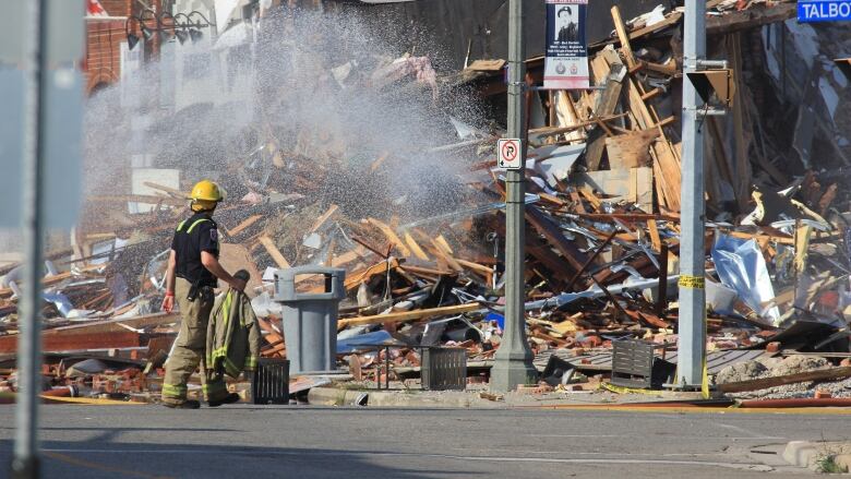 Water is sprayed on a huge pile of rubble on a street corner as a firefighter looks on.