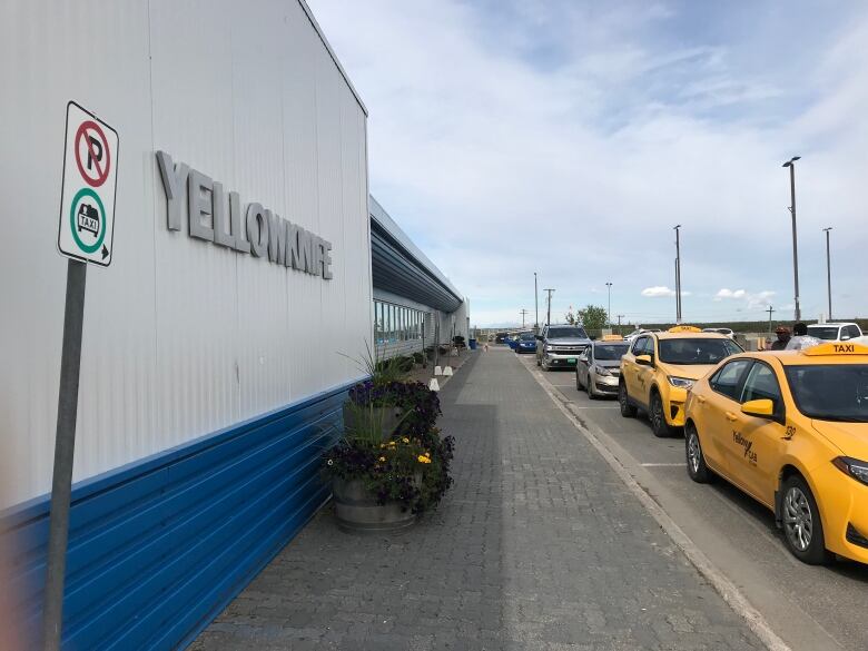 Yellow cars line up in front of a building on a sunny day. 