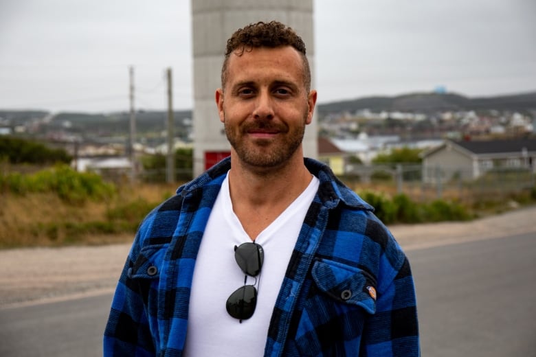 A man wearing a white t-shirt and blue flannel jacket smiles.