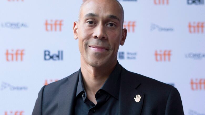 A Black man wearing a black suit is standing in front of a sign for TIFF