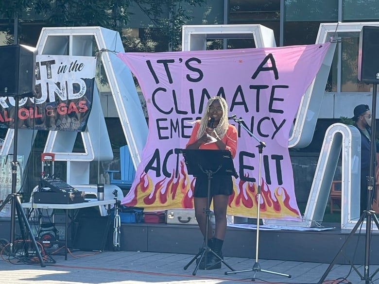 A person stands at a podium on a stage in front of the Hamilton sign, which is draped in climate banners.