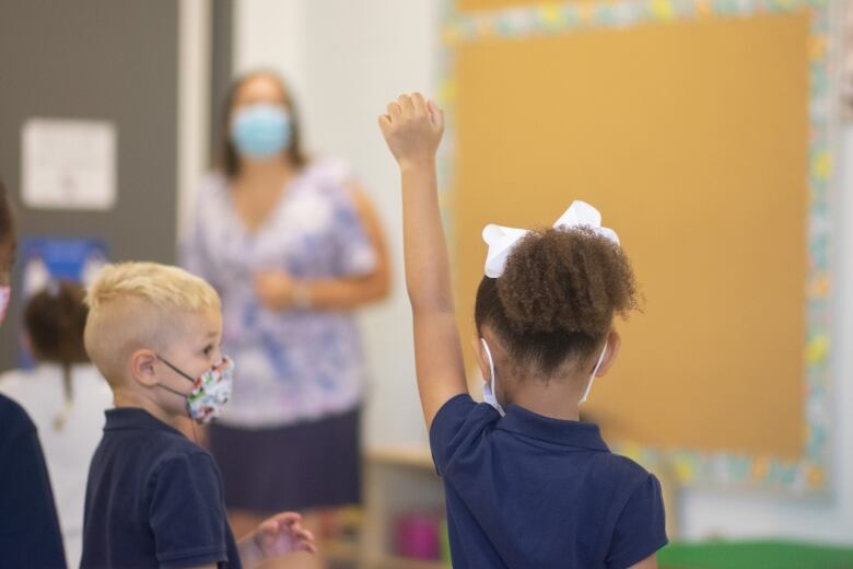 A kindergarten student wearing a mask at Sts. Peter & Paul Catholic Elementary School in Hamilton raises her hand in class. 