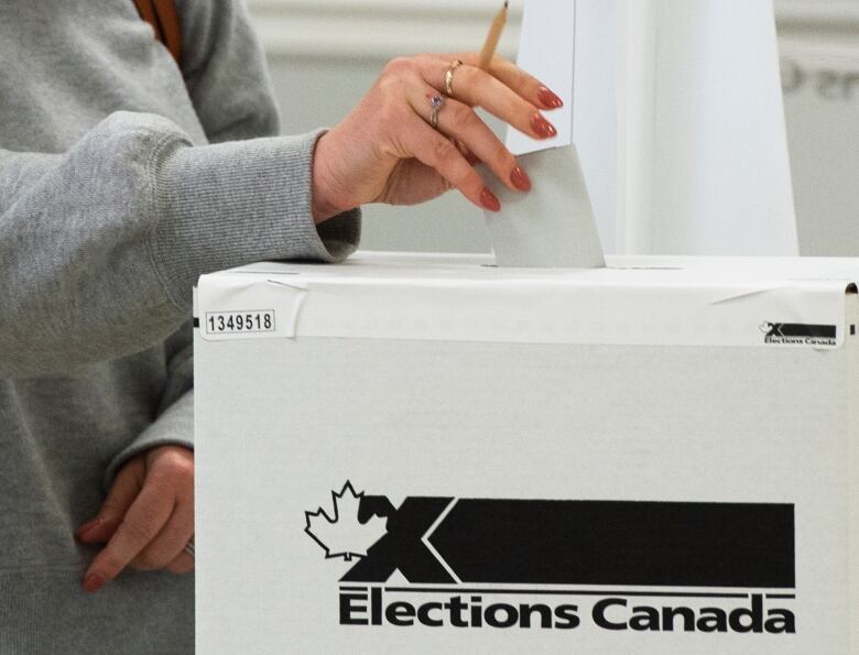 A person puts a ballot into the top of a ballot box.