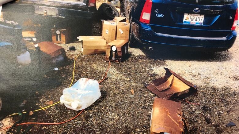 Plastic jugs and cardboard boxes with jugs inside scattered on the ground. Some of the cardboard appears to be soaked with oil.