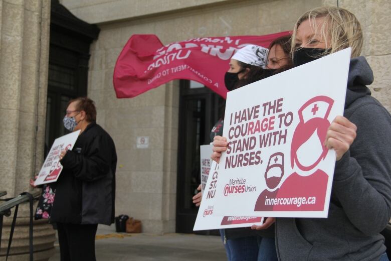 A woman in a grey sweater holds a white signs that reads, 