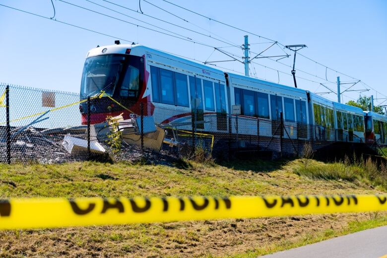 A red-and-white train is parked on train tracks on a sunny day while yellow tape with the word 