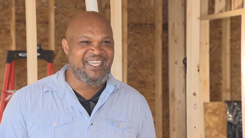 A Black man wearing a light blue shirt standing in an unfinished house