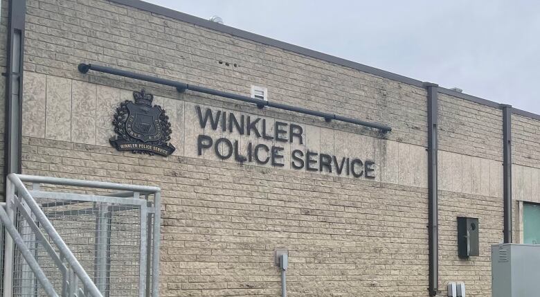 The exterior of a grey brick building shows a 'Winkler Police Service' sign.