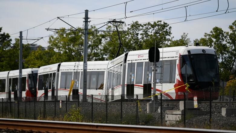 A red and white light rail train rests on the tracks after a minor derailment.