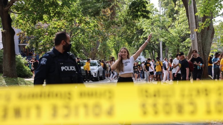 A young woman smiles jubilantly in the middle of a street, behind police tape. A crowd stands behind her and a police officer looks at her.