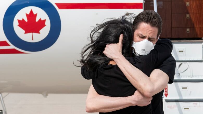 A man and woman hug tightly at the bottom of an airplane's ramp.