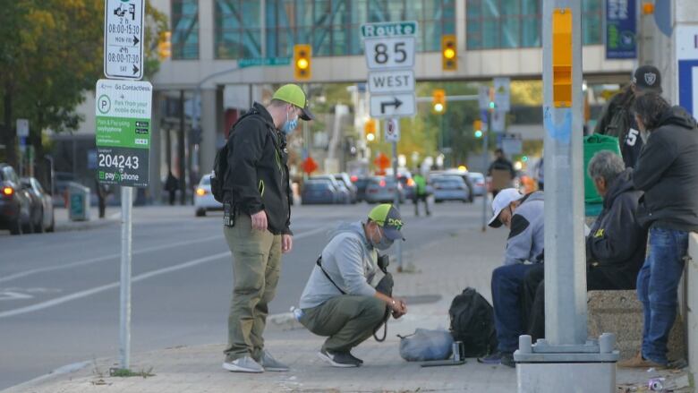 People wearing green hats are standing on a sidewalk talking to a group of people.