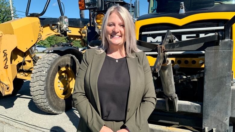 Nova Scotia Public Works Minister Kim Masland smiles in front of yellow and black construction vehicles.