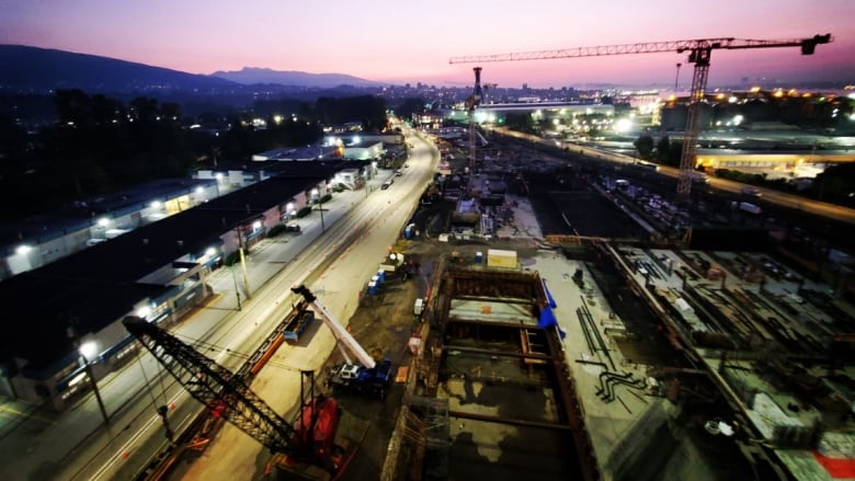 A construction site with a crane in the background and heavy equipment with a sunset in the background shows the very early stages of the building of the plant.