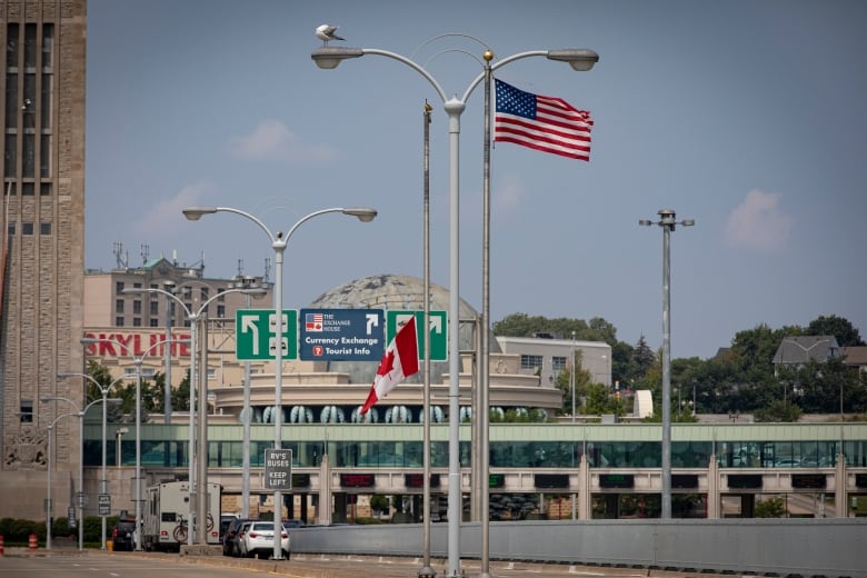 a canadian and american flag are seen flying at a border crossing with a bridge