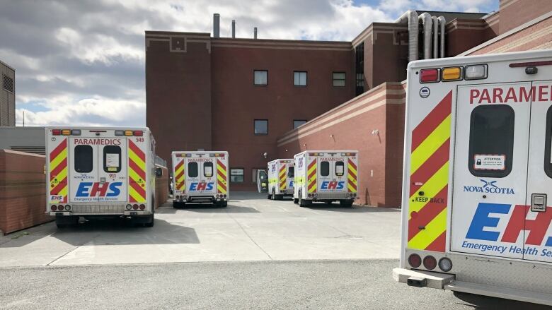 Five ambulance vehicles are parked outside a brick hospital building.