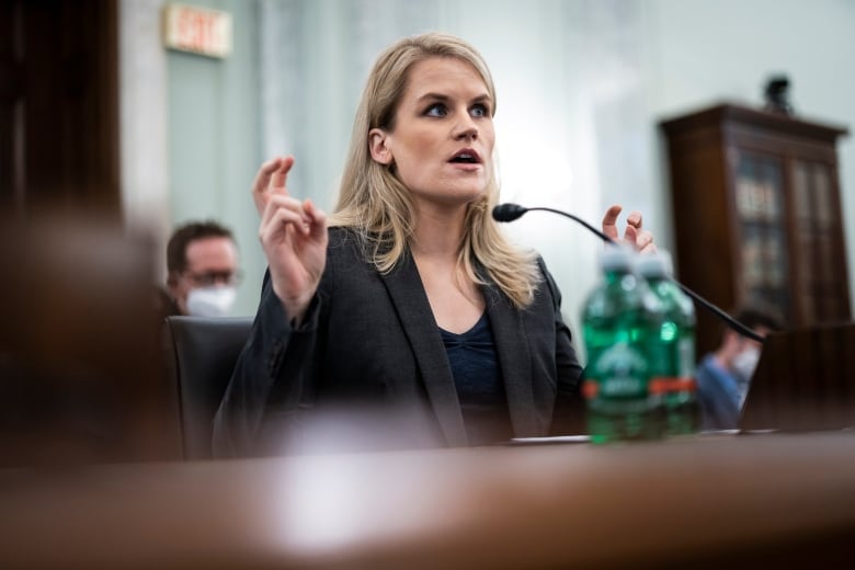 Woman holds up her hands gesturing with air quotes as she speaks at a table