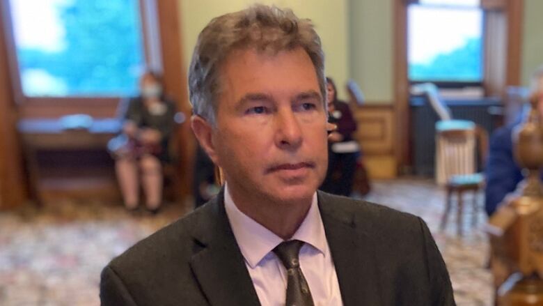 A man wearing a suit jacket, collared shirt and tie looks off in the distance.