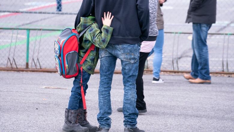 A young child clings to parent in schoolyard.