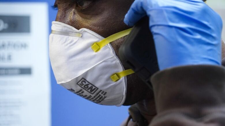 A person wearing blue latex gloves and a white N95 mask.