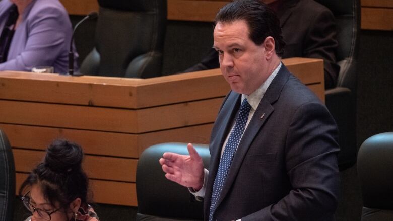 A man stands speaking in a territorial legislature.