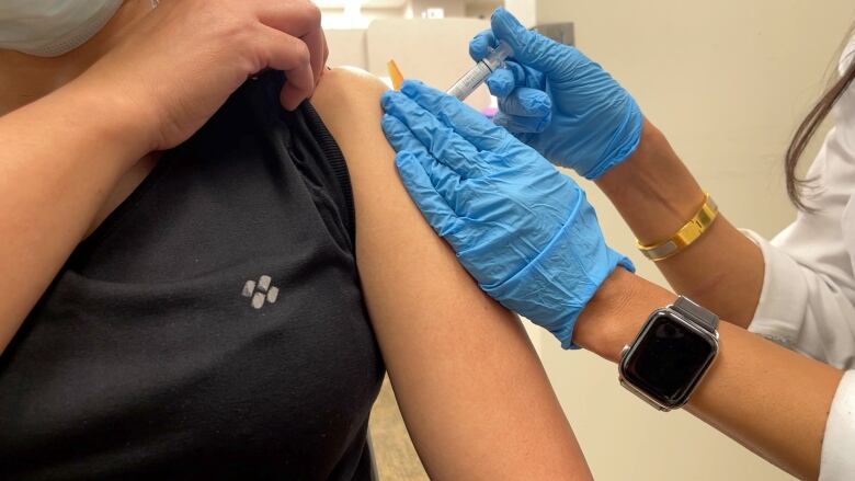 A pharmacist, wearing blue disposable gloves, injects a person with the flu vaccine.