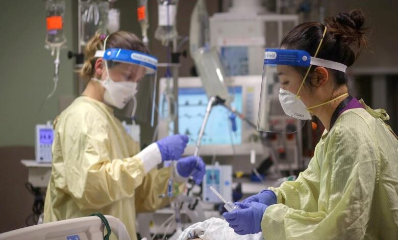 Health care workers in masks and face shields care for a patient in the ICU