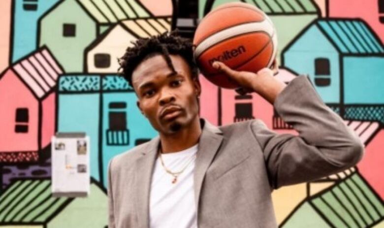 A man holding a basketball stands in front of an outdoor wall mural. 