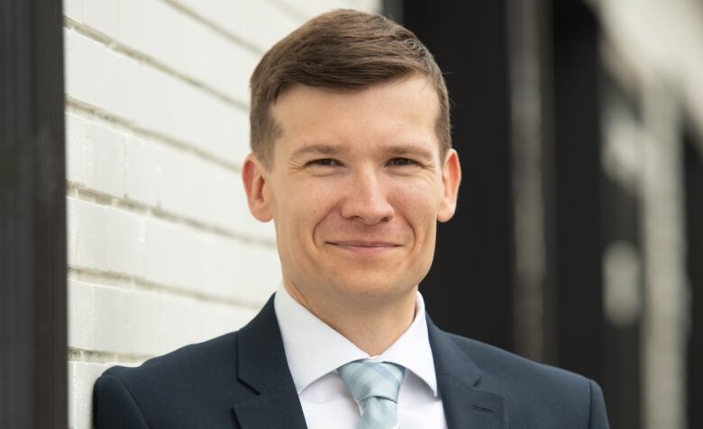 A close-up shot of a man in a suit, smiling at the camera.