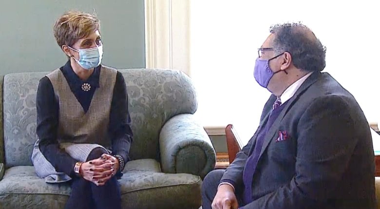 Two people converse while wearing masks.