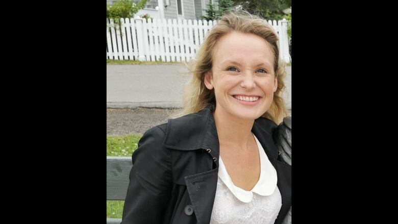 A woman with blonde hair, a black jacket and white lace blouse smiles.