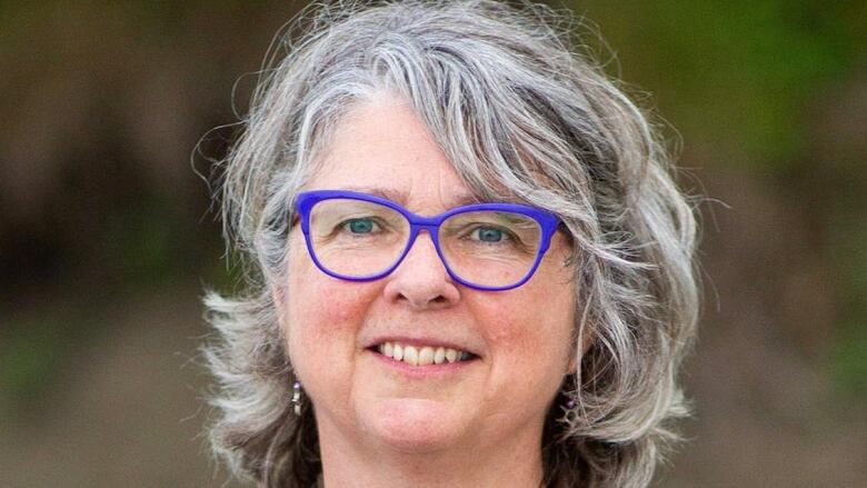 Close up portrait of a smiling grey haired woman with bright blue rimmed glasses