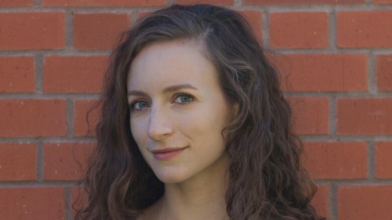 Close up portrait of a woman with long curly brown hair she is standing in front of a brick wall and smiling