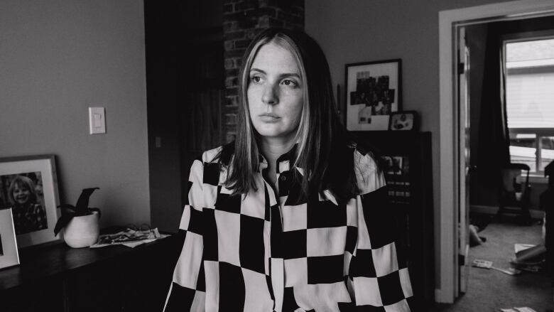 Black and white portrait of a woman with shoulder length hair wearing a checkered jacket and standing in a living room