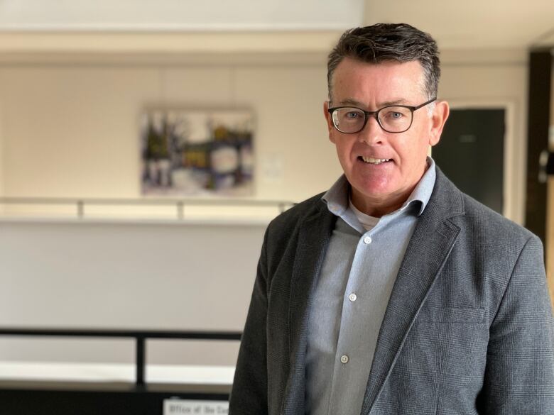 A man with glasses and suit smiles.