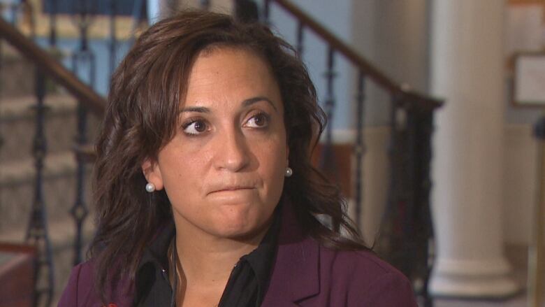 A woman with dark hair is wearing a maroon blazer with a poppy on the blazer