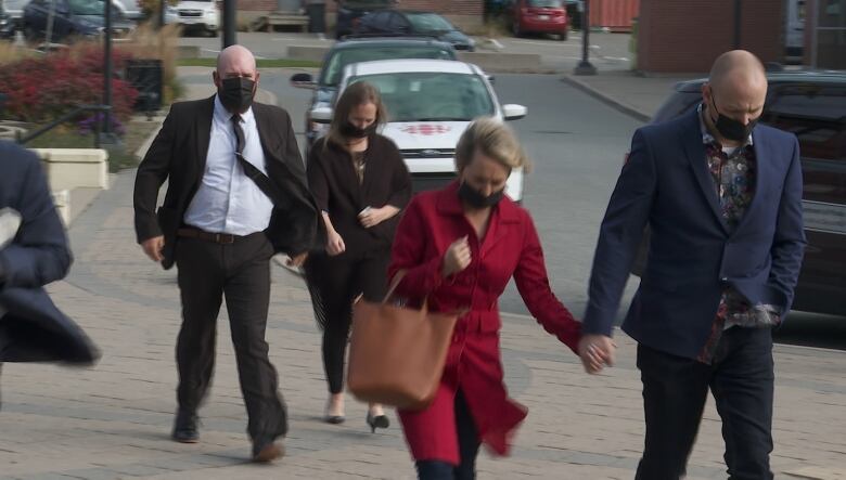 Two couples, everyone wearing face masks, walk toward the camera. The couple in the foreground is holding hands. 