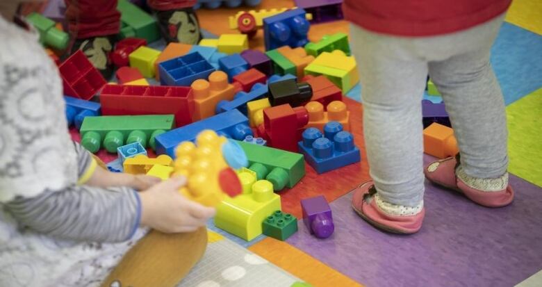 Two unidentifiable children stand amongst Duplo blocks.  